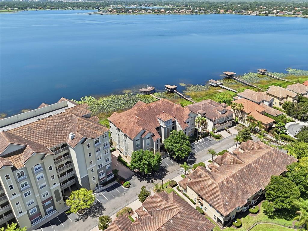 An aerial view shows several multi-story residential buildings situated along the shore of a lake — 8767 THE ESPLANADE UNIT 40, ORLANDO, FL