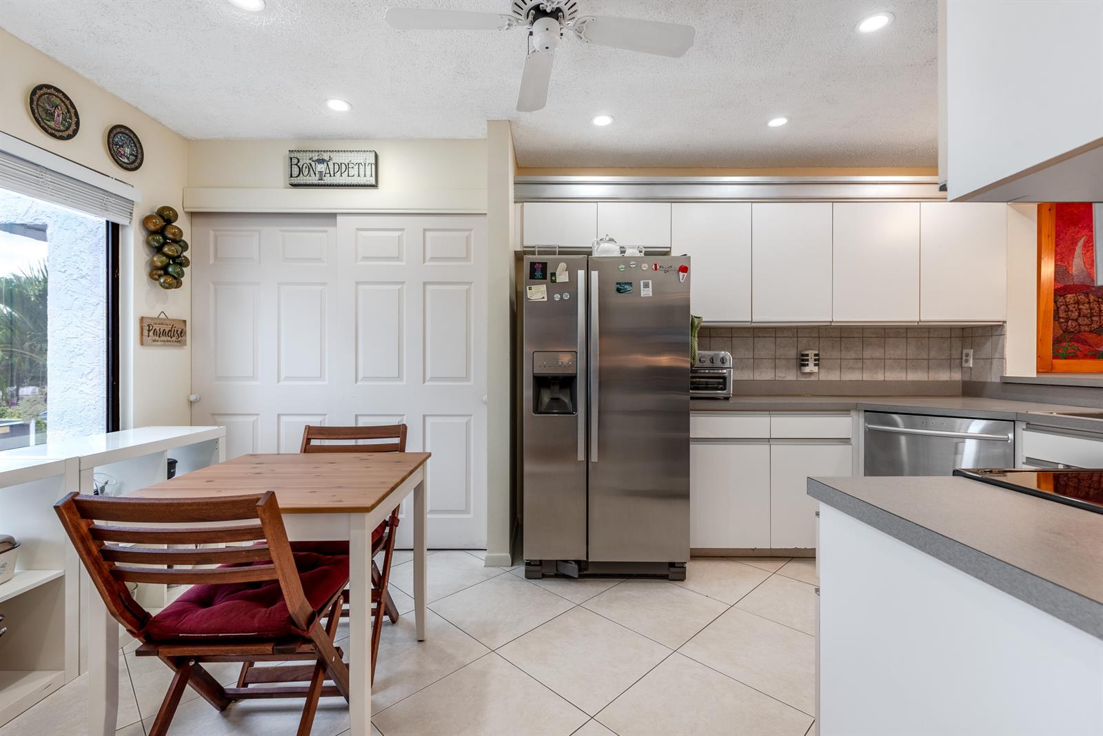 A kitchen features white cabinets, stainless steel appliances, a dining table, and tile flooring — 7689 Glendevon Lane # 1807, Delray Beach FL 33446, DELRAY BEACH, FL