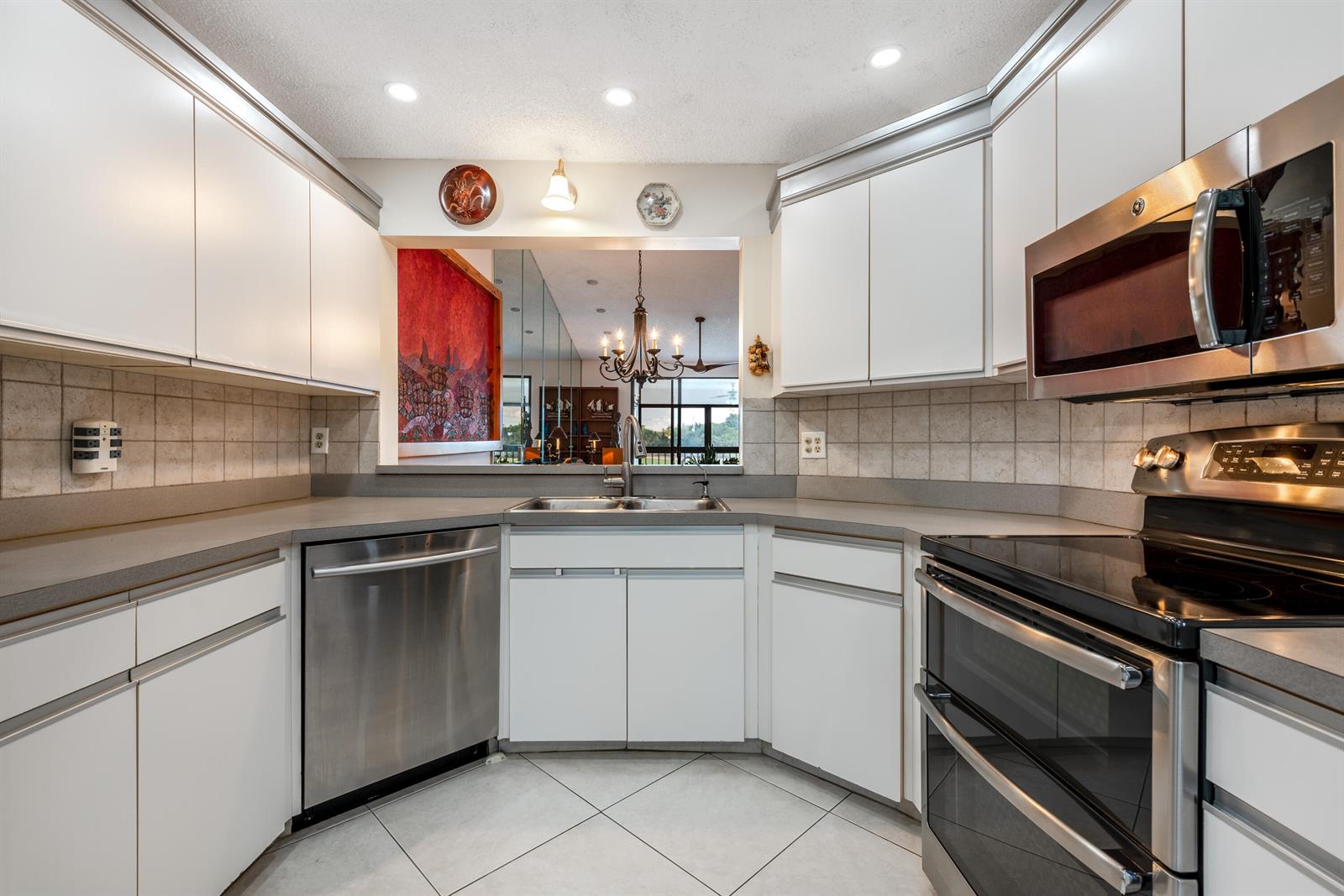 A kitchen with white cabinets, stainless steel appliances, gray countertops, and a pass-through window — 7689 Glendevon Lane # 1807, Delray Beach FL 33446, DELRAY BEACH, FL