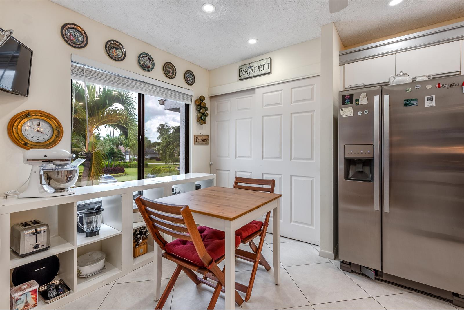 A kitchen dining area features a small wooden table, white shelving, and a stainless refrigerator — 7689 Glendevon Lane # 1807, Delray Beach FL 33446, DELRAY BEACH, FL