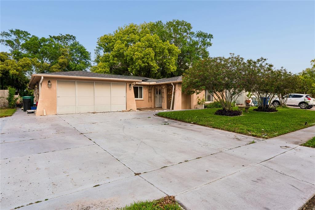 A single-story house with a large concrete driveway, a two-car garage, and mature trees — 3122 BAHIA AVENUE, HOLIDAY, FL