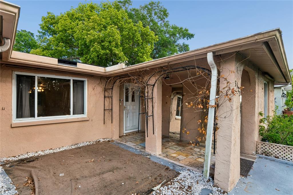 A tan stucco house exterior features a covered entryway with a metal trellis and walkway — 3122 BAHIA AVENUE, HOLIDAY, FL
