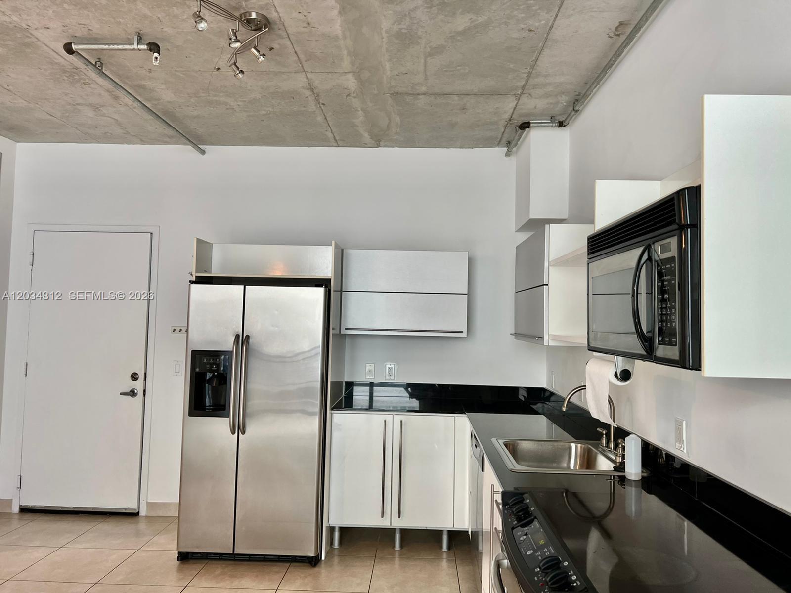 A kitchen features stainless steel appliances, white cabinets, black countertops, and an exposed concrete ceiling — 690 SW 1st Ct # 1026, Miami FL 33130, MIAMI, FL