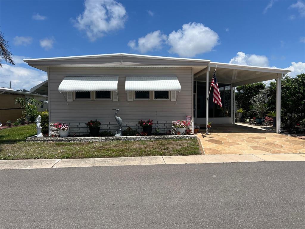 A single-story manufactured home features light siding, white window awnings, and a paved carport — 29250 US HIGHWAY 19 N UNIT 622, CLEARWATER, FL