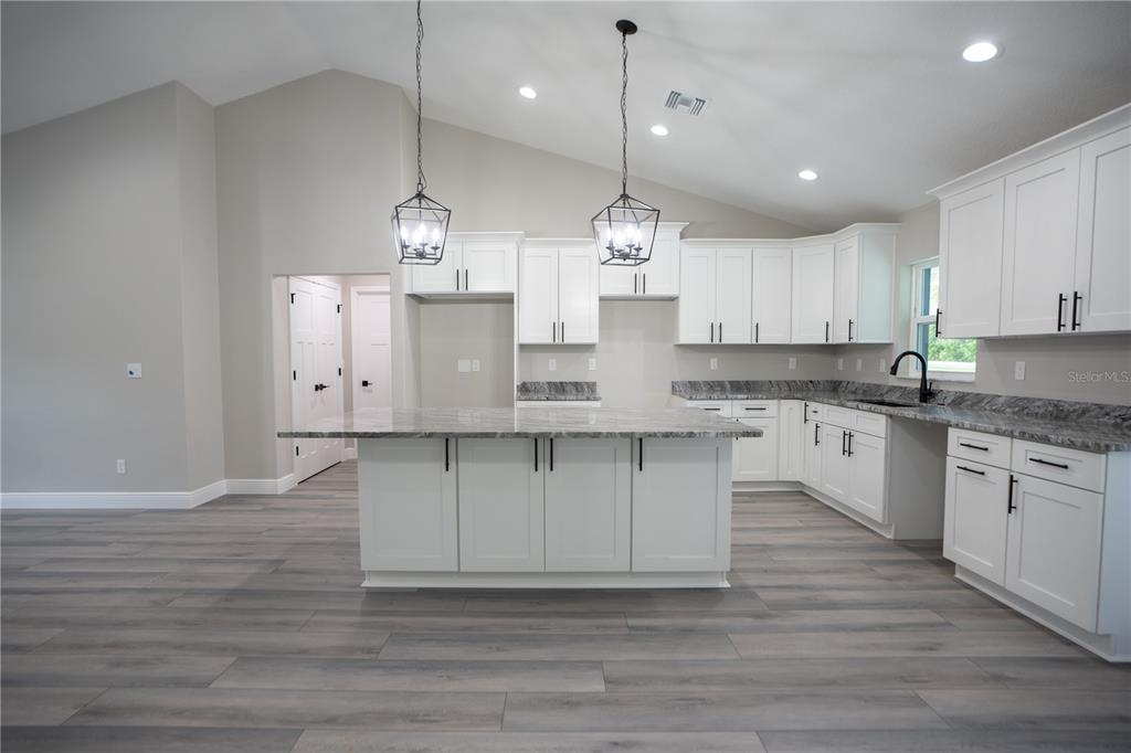 A kitchen with white cabinets, a granite island, and gray wood-look flooring under vaulted ceilings — 6689 SW 179TH COURT ROAD, DUNNELLON, FL