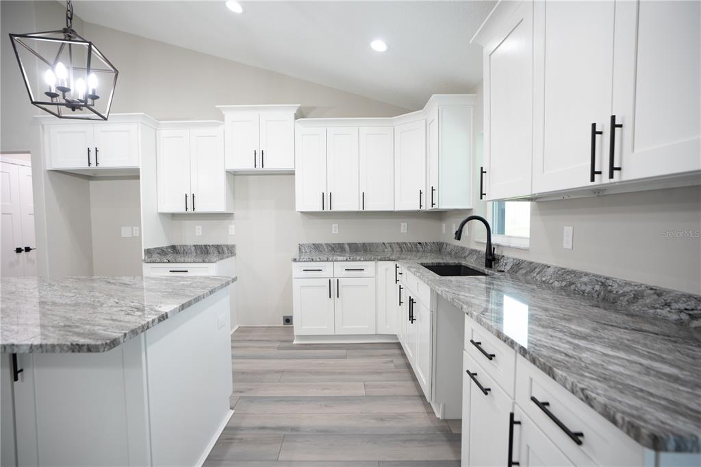 A modern kitchen features white cabinets, granite countertops, a kitchen island, and wood-look flooring — 6689 SW 179TH COURT ROAD, DUNNELLON, FL