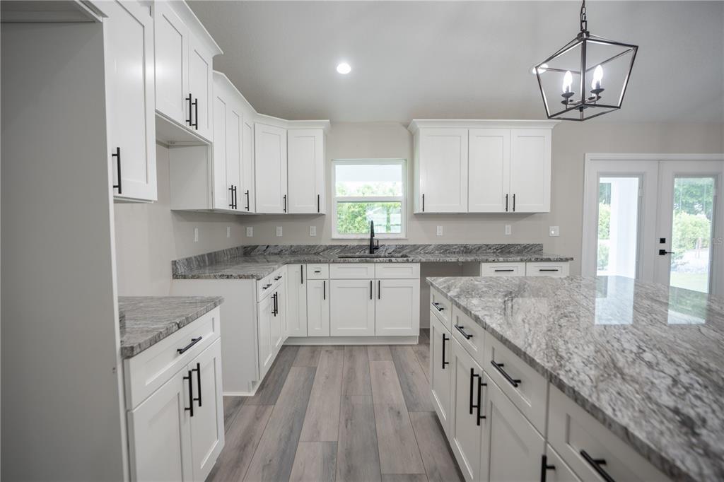 A kitchen features white cabinets, granite countertops, a large island, and wood-look flooring — 6689 SW 179TH COURT ROAD, DUNNELLON, FL