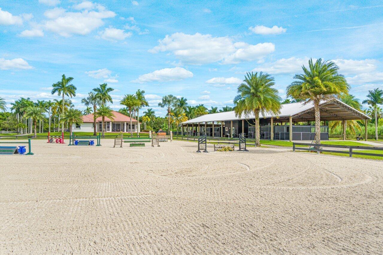 An outdoor horse riding arena with jumps, a stable building, and palm trees — 2587 Skipiks Way, Wellington FL 33470, WELLINGTON, FL
