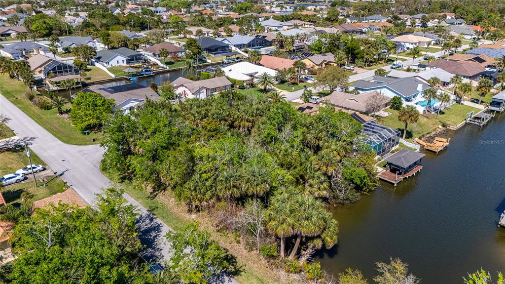 An aerial view shows a wooded vacant lot situated between a residential street and a canal — 2 COCONUT COURT, PALM COAST, FL