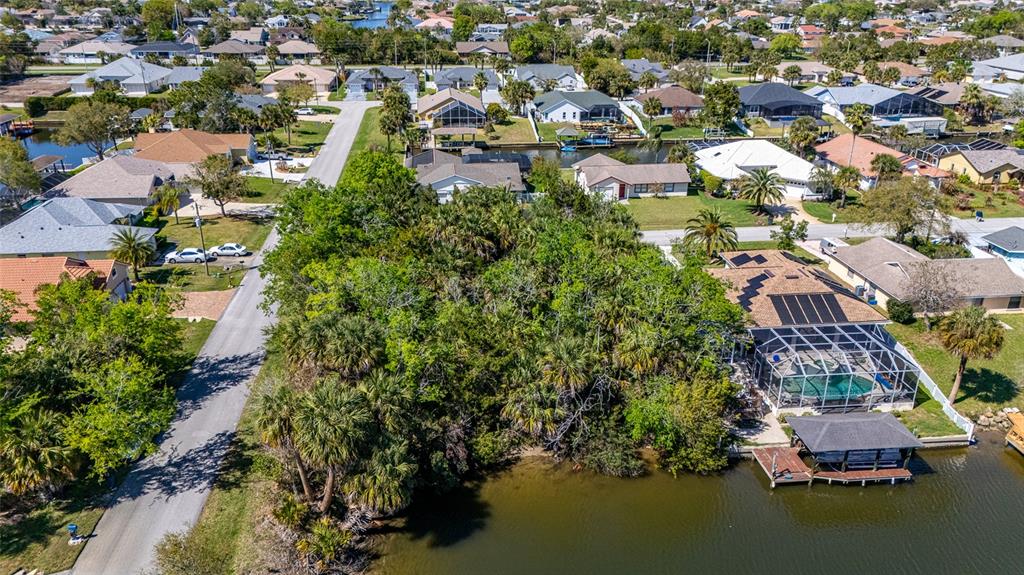 An aerial view shows a wooded waterfront lot situated between residential houses and a canal — 2 COCONUT COURT, PALM COAST, FL