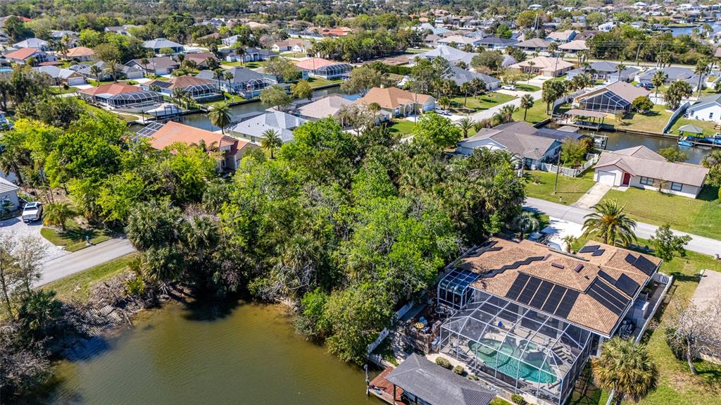 An aerial view shows a suburban neighborhood with houses, a canal, and a pool enclosure — 2 COCONUT COURT, PALM COAST, FL