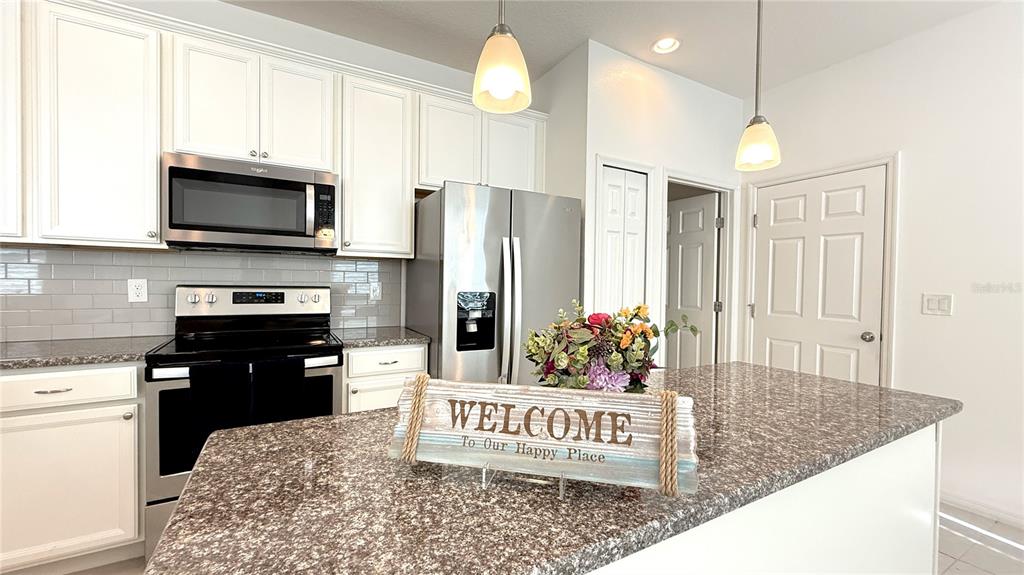 A kitchen features white cabinets, stainless steel appliances, granite countertops, and a central island — 2636 SEDGE GRASS WAY, ORLANDO, FL