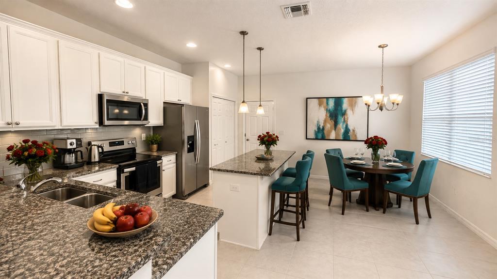 A kitchen with white cabinets, granite countertops, and an adjacent dining area with teal chairs — 2636 SEDGE GRASS WAY, ORLANDO, FL