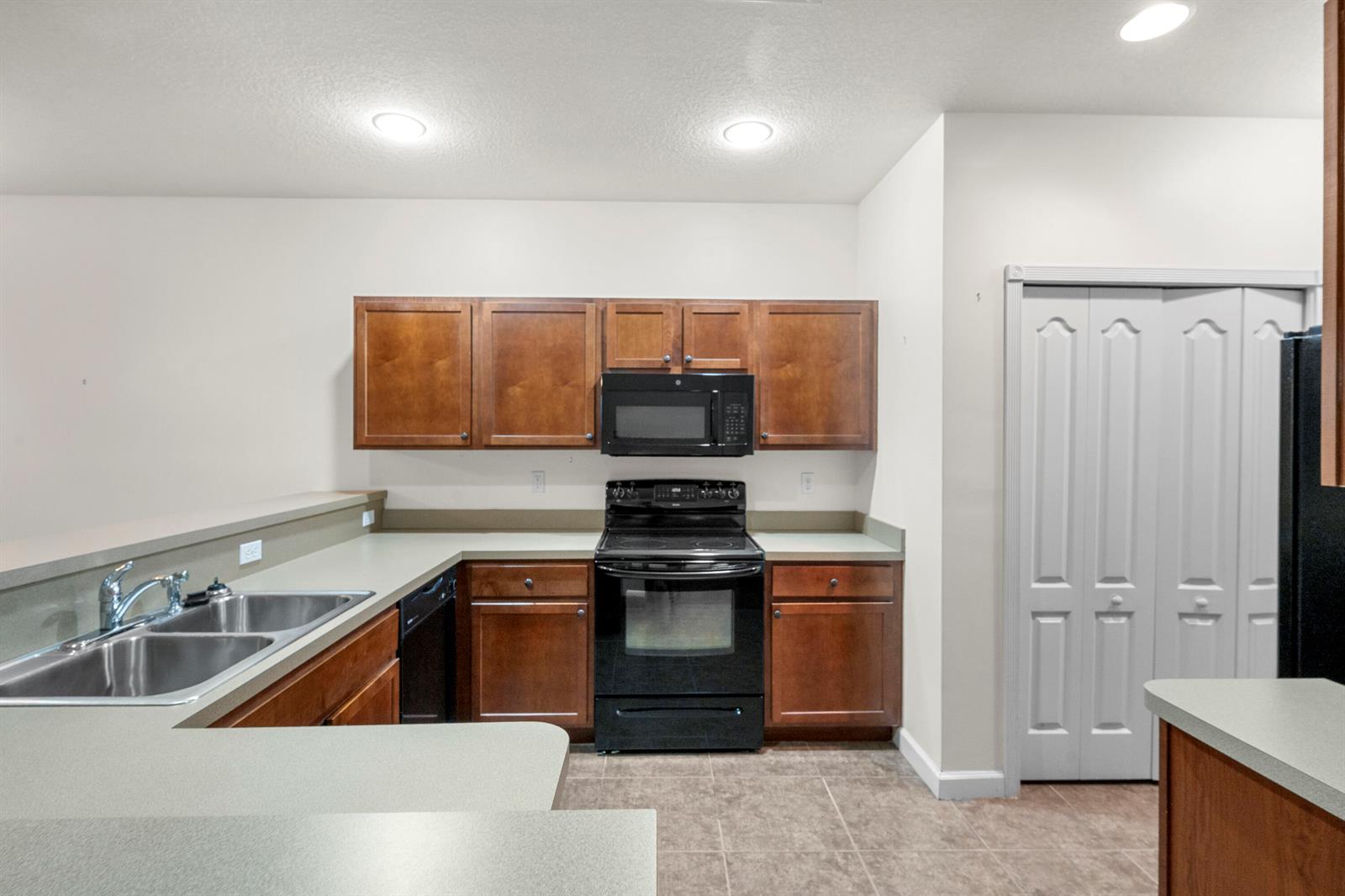 A kitchen features wood cabinets, black appliances, a double sink, and light-colored countertops — 2545 Creekside Drive, Fort Pierce FL 34981, FORT PIERCE, FL