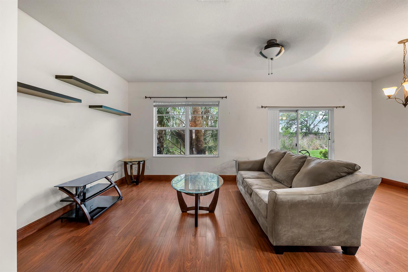 A living room features wood-look flooring, a grey sofa, a glass coffee table, and floating shelves — 2545 Creekside Drive, Fort Pierce FL 34981, FORT PIERCE, FL