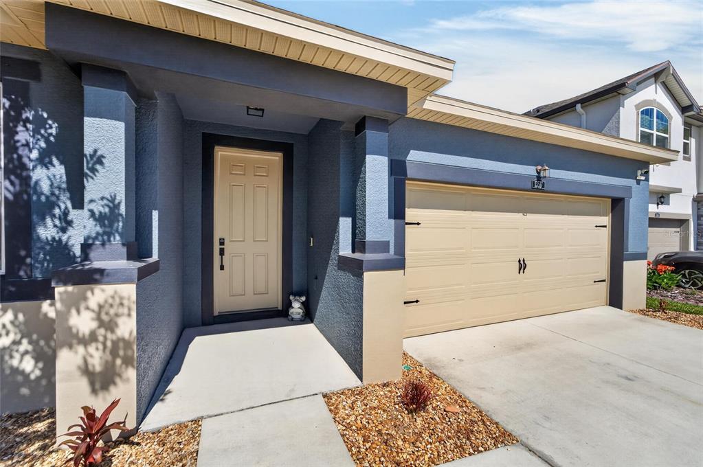 A blue stucco house exterior features a beige front door and a two-car garage — 13517 TEXAS SAGE PLACE, RIVERVIEW, FL