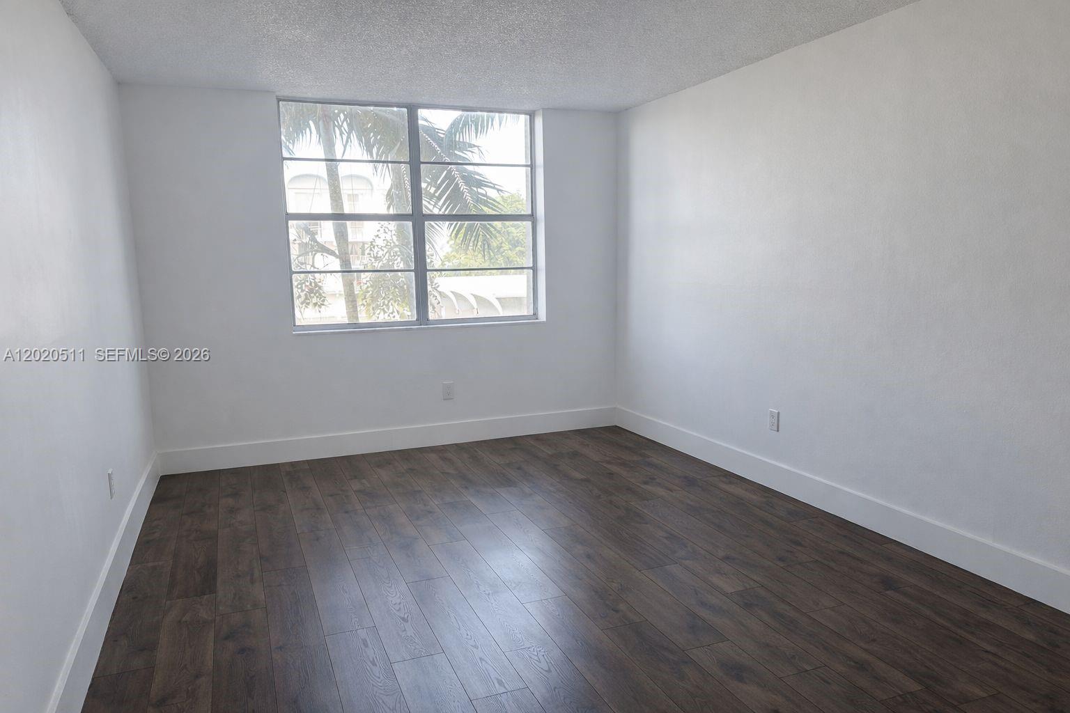 An empty room features white walls, dark wood-look flooring, and a large window — 496 NW 165th # 412, Miami FL 33169, MIAMI, FL