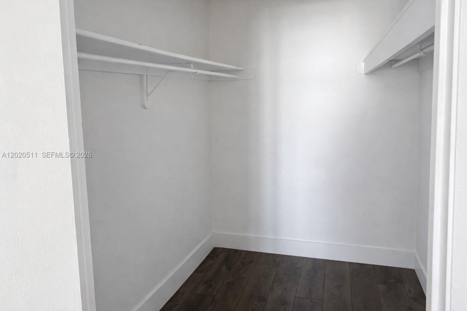 A walk-in closet features white walls, dark wood-look flooring, and built-in shelving — 496 NW 165th # 412, Miami FL 33169, MIAMI, FL