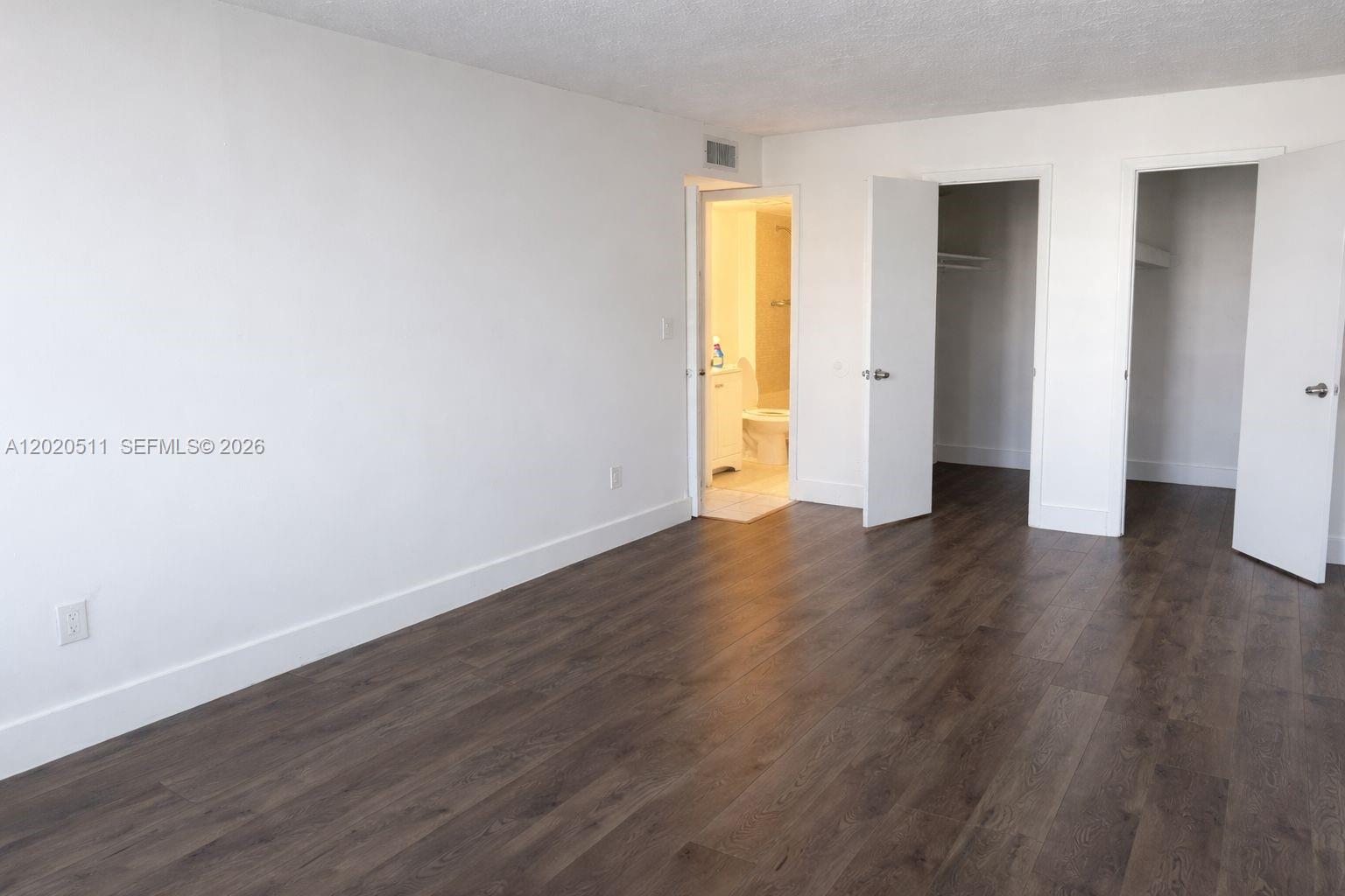 A bedroom with white walls, dark wood-look flooring, two closet doors, and an attached bathroom — 496 NW 165th # 412, Miami FL 33169, MIAMI, FL