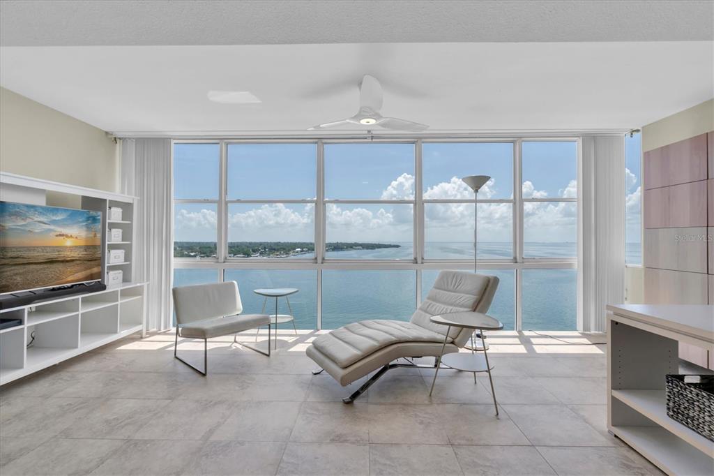 A living room with tile floors, white furniture, and floor-to-ceiling windows overlooking the ocean — 7200 SUNSHINE SKYWAY LN S UNIT 15H, ST PETERSBURG, FL