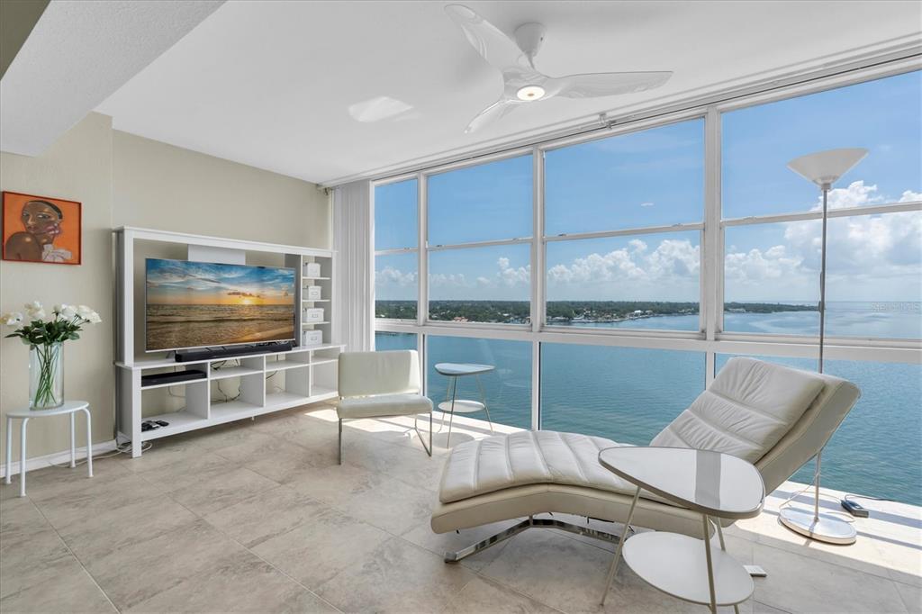 A living room features white furniture, tile floors, and floor-to-ceiling windows overlooking the water — 7200 SUNSHINE SKYWAY LN S UNIT 15H, ST PETERSBURG, FL