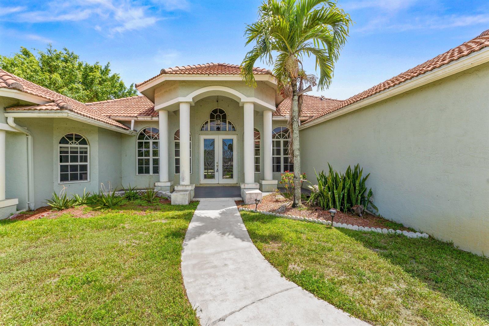 A light green house features a columned entryway, arched windows, and a tiled roof — 19482 Green Grove Court, FL 33470, FL