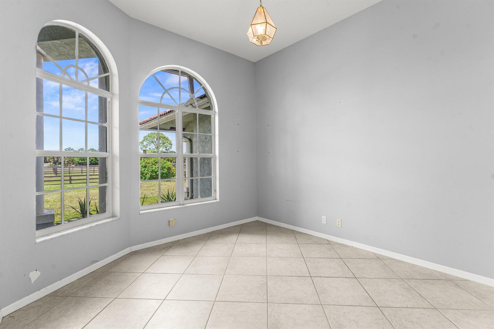 An empty room features light gray walls, tile flooring, and two large arched windows — 19482 Green Grove Court, FL 33470, FL