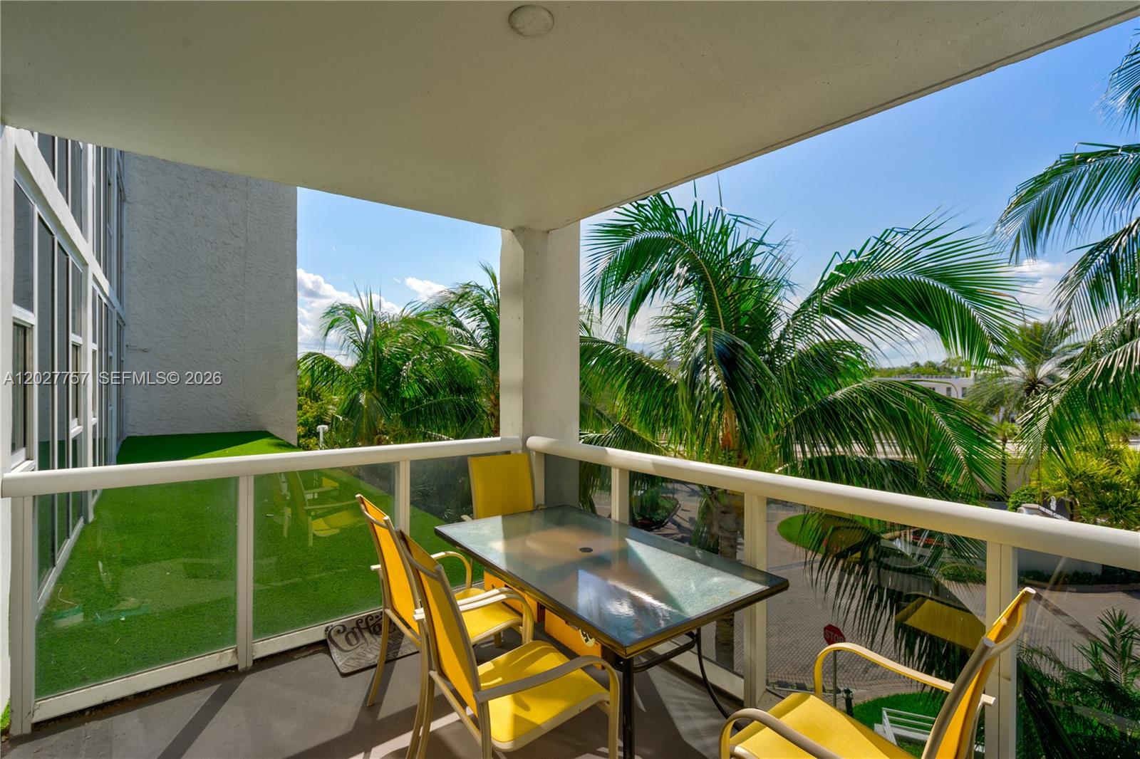 A balcony features a glass-topped table, yellow chairs, and views of palm trees — 10275 Collins Ave # 223, Bal Harbour FL 33154, BAL HARBOUR, FL