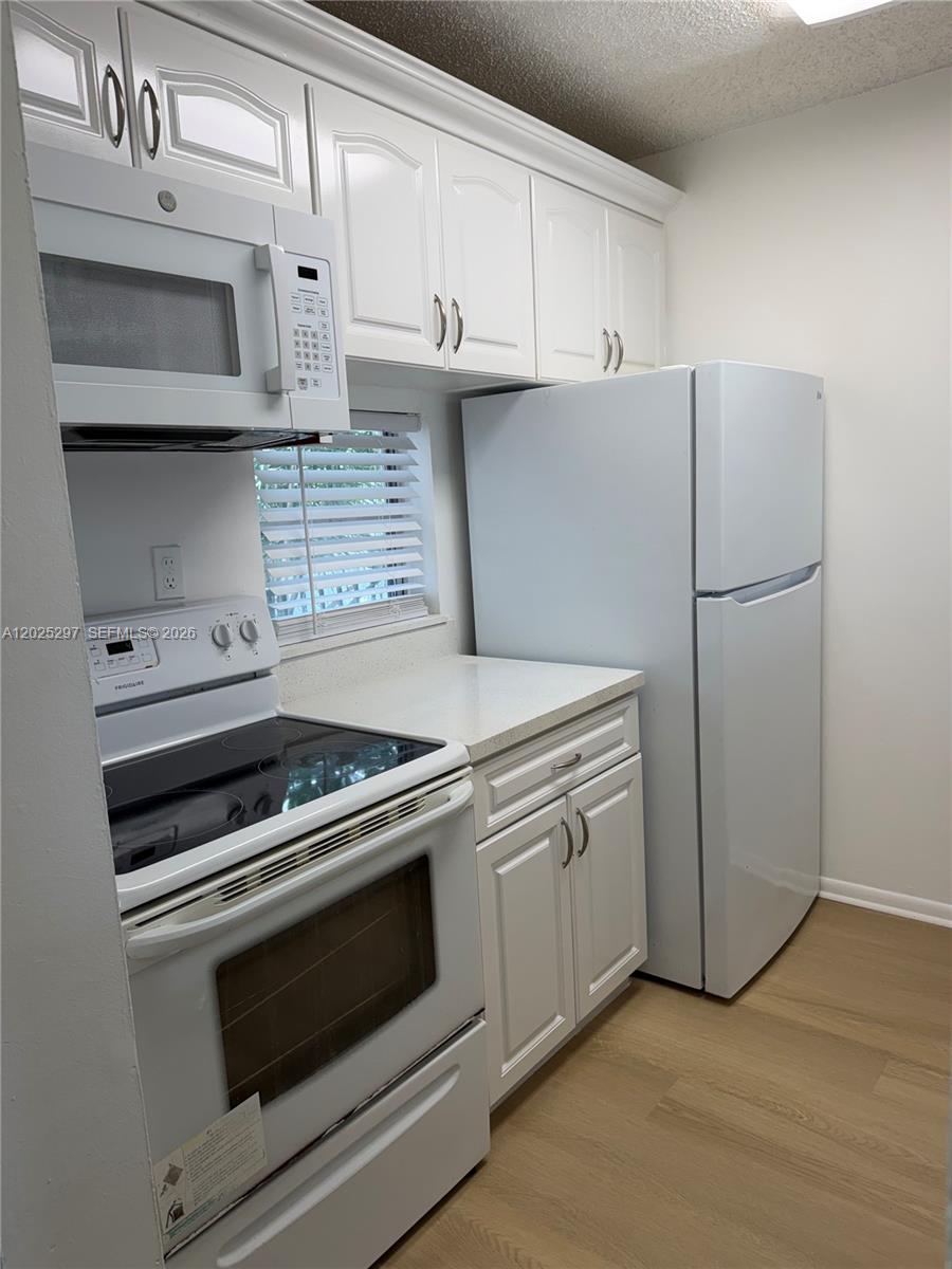 A kitchen features white cabinets, white appliances, a window with blinds, and light wood flooring — 8560 N Sherman Cir # 404, Miramar FL 33025, MIRAMAR, FL