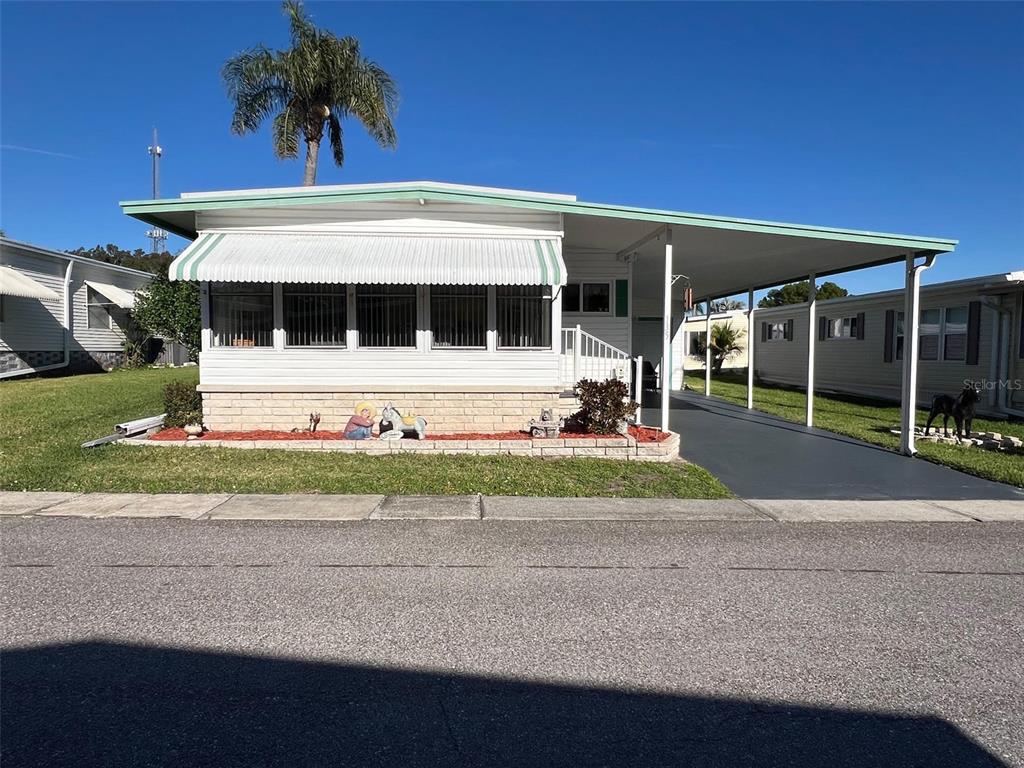 A white mobile home with a green-trimmed awning and an attached carport sits on grass — 29250 US HIGHWAY 19 N UNIT 135, CLEARWATER, FL