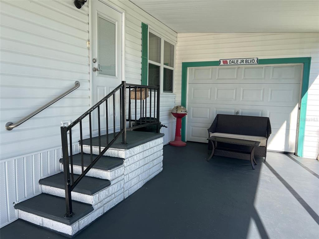 A covered porch features a set of stairs with a handrail and a small seating area — 29250 US HIGHWAY 19 N UNIT 135, CLEARWATER, FL