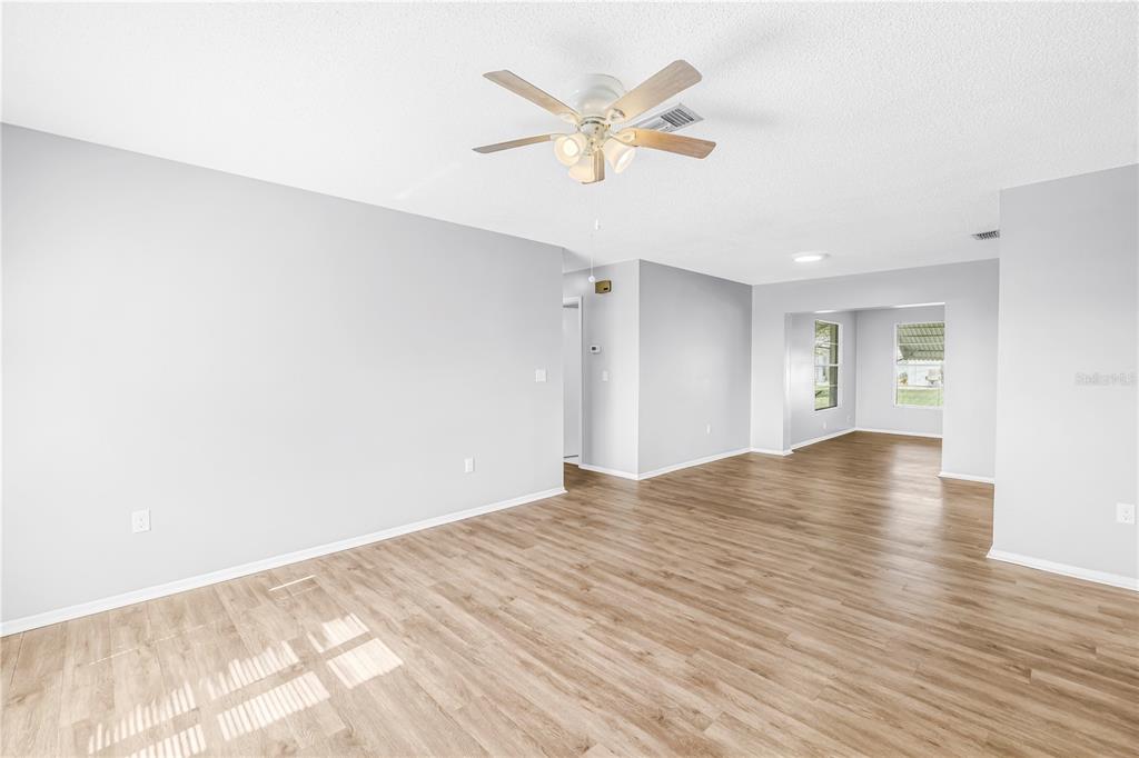 An empty living room with light gray walls, wood-look flooring, and a ceiling fan — 802 BUTTONWOOD DRIVE, BRADENTON, FL