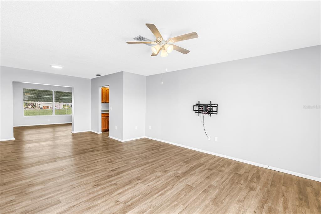 An empty living room with light wood-look flooring, gray walls, and a ceiling fan — 802 BUTTONWOOD DRIVE, BRADENTON, FL