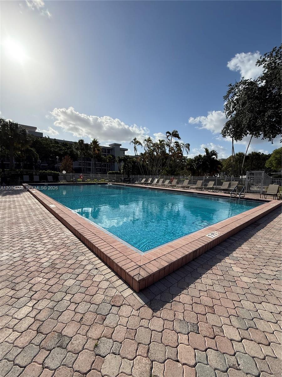 A rectangular outdoor swimming pool is surrounded by a brick paver deck and lounge chairs — 2691 S Course Dr # 202, Pompano Beach FL 33069, POMPANO BEACH, FL