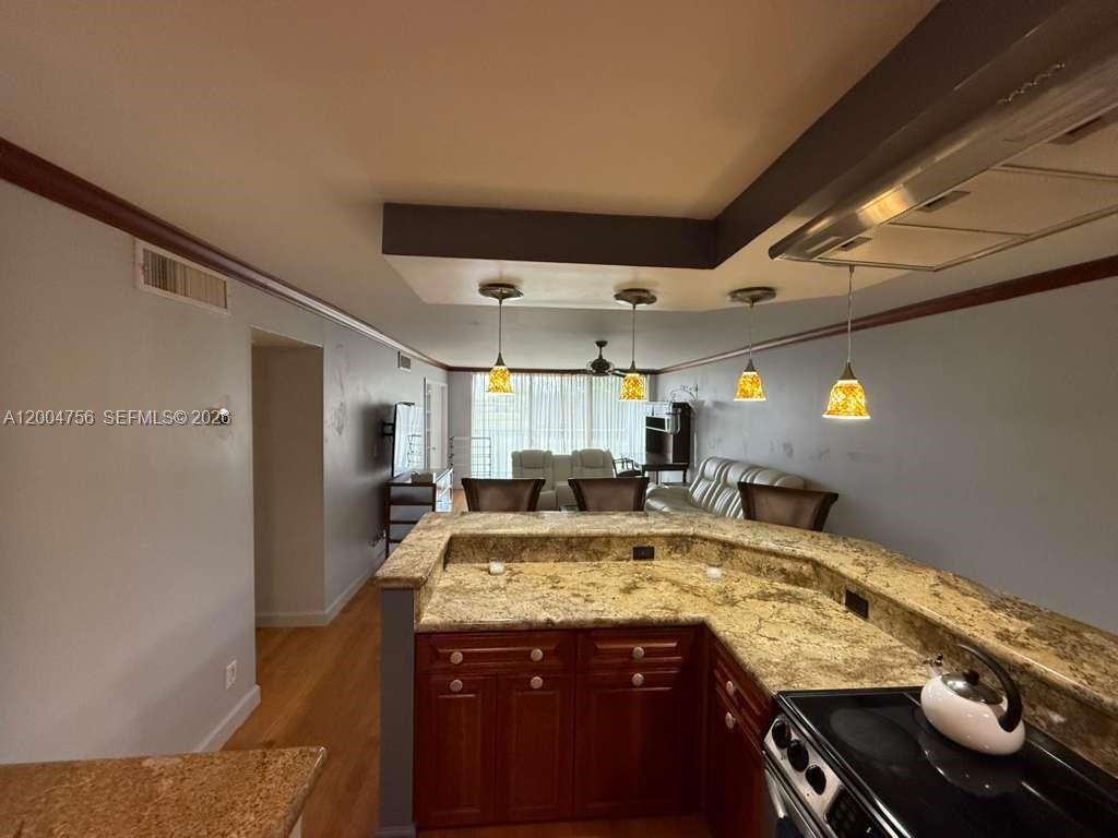 A kitchen with granite countertops and wooden cabinets overlooks a living room with pendant lights — 2691 S Course Dr # 202, Pompano Beach FL 33069, POMPANO BEACH, FL