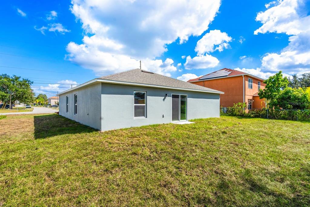 The exterior rear view of a single-story house with a gray stucco finish and yard — 1822 BERING ROAD, KISSIMMEE, FL