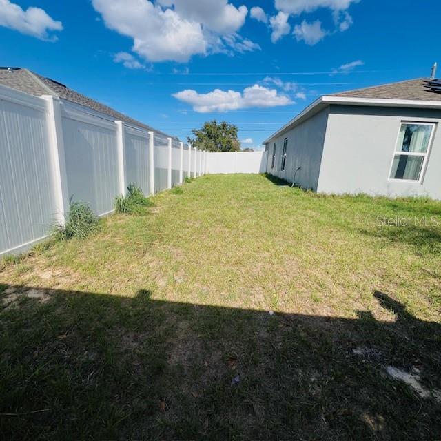 A grassy side yard sits between a white vinyl fence and the side of a house — 1822 BERING ROAD, KISSIMMEE, FL