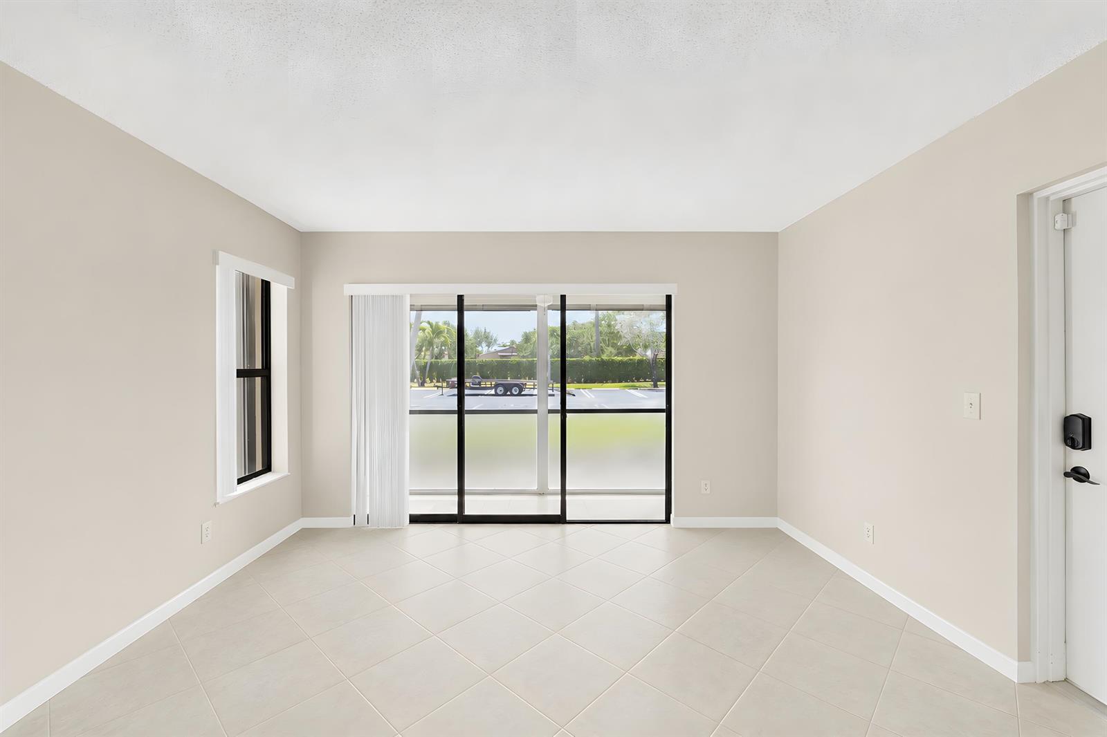 An empty room with beige walls, tile flooring, a sliding glass door, and a window — 821 Sky Pine Way # D1, FL 33415, FL