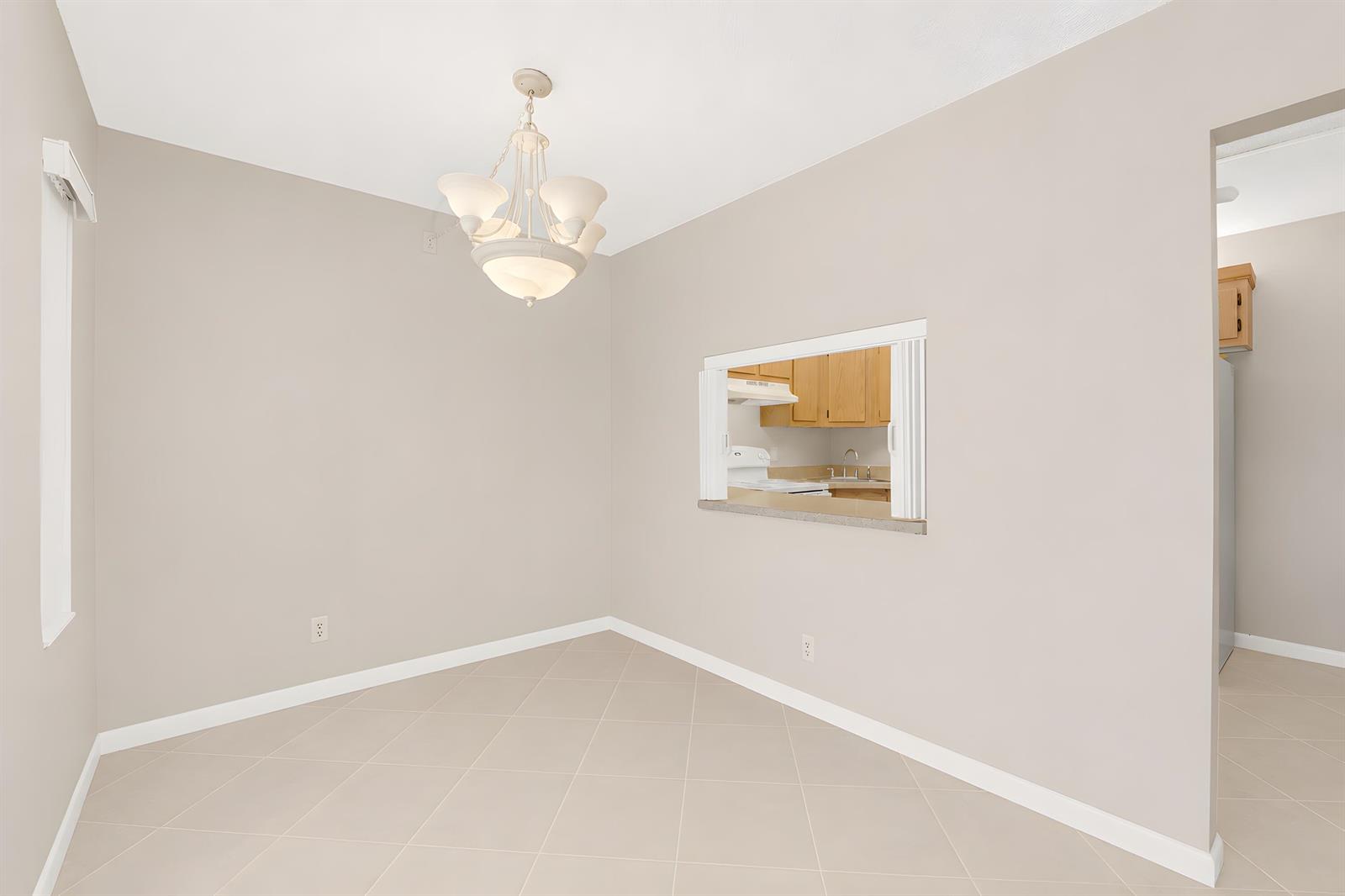 A dining area with beige walls, tile flooring, a chandelier, and a kitchen pass-through window — 821 Sky Pine Way # D1, FL 33415, FL