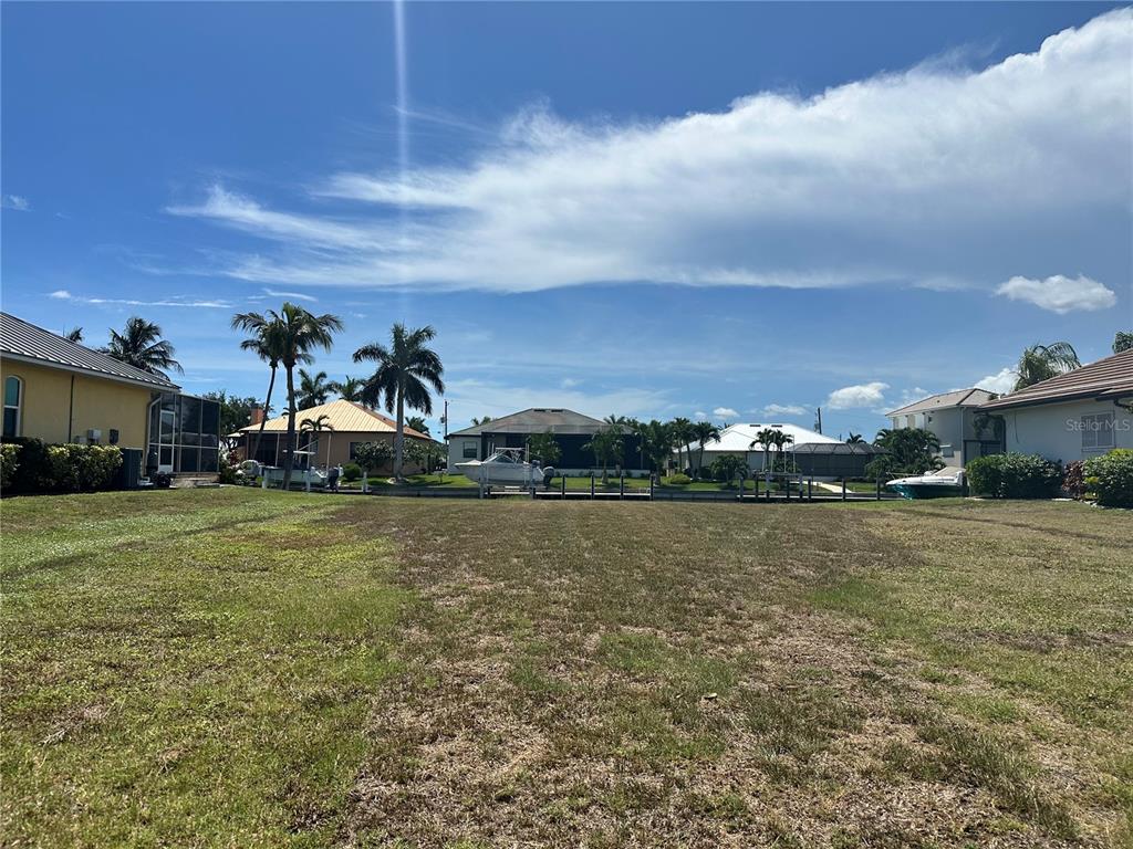 A vacant grassy lot faces a canal with boat docks and neighboring houses in the background — 3611 BONAIRE COURT, PUNTA GORDA, FL