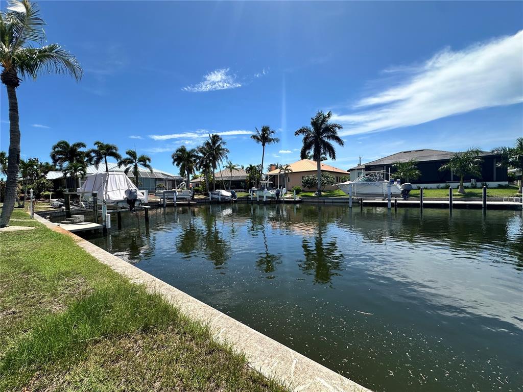 A canal view features several boat docks with covered vessels and palm trees under blue skies — 3611 BONAIRE COURT, PUNTA GORDA, FL