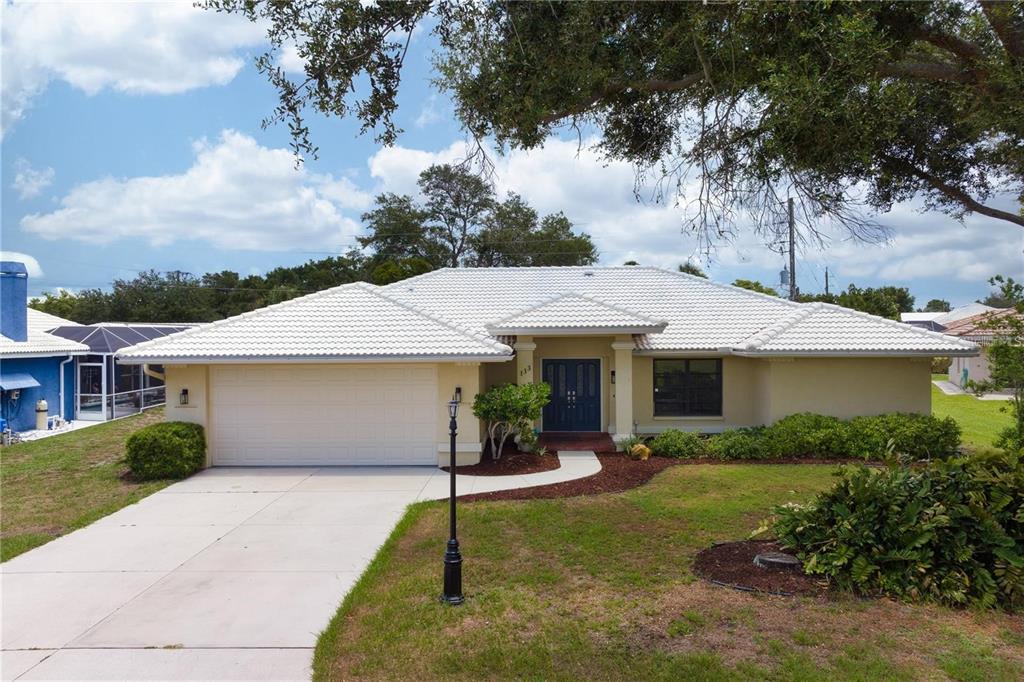 A single-story house with a white tile roof, beige stucco walls, and a two-car garage — 133 1ST AVENUE, NOKOMIS, FL