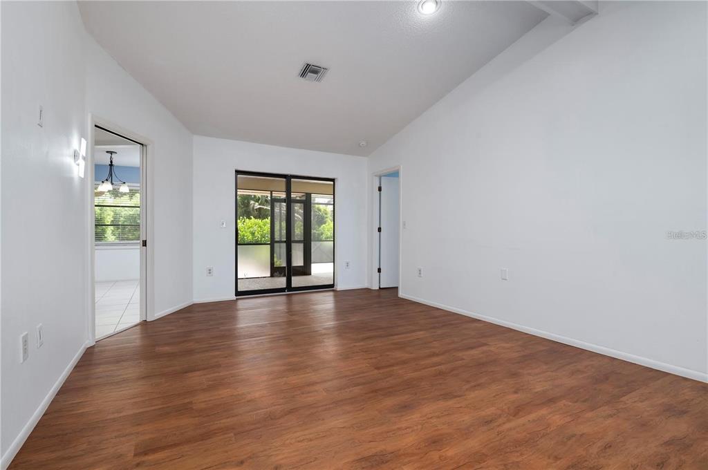 An empty room with wood-look flooring, white walls, and sliding glass doors to a patio — 133 1ST AVENUE, NOKOMIS, FL