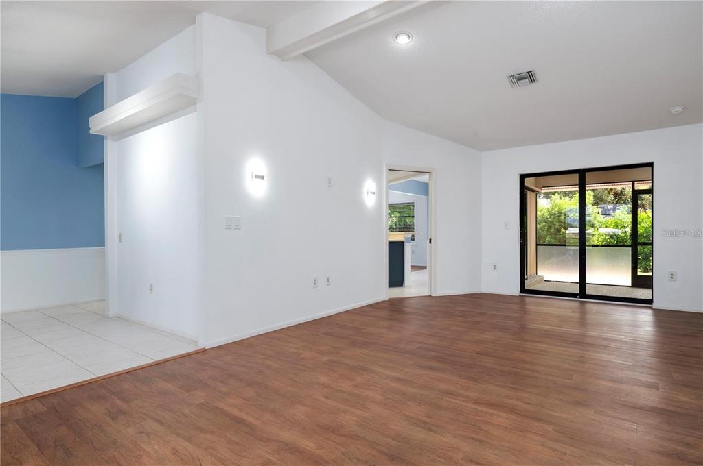 A living room with wood-look flooring, white walls, and a sliding glass door to a patio — 133 1ST AVENUE, NOKOMIS, FL