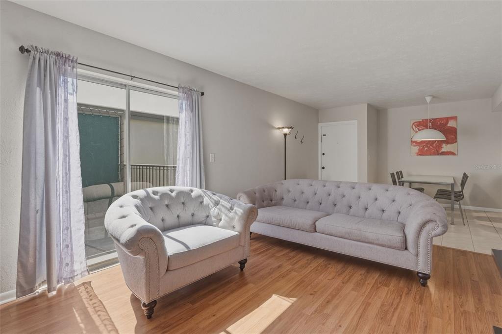 A living room features light gray tufted furniture, wood-look flooring, and a sliding glass door — 1799 N HIGHLAND AVENUE UNIT 114, CLEARWATER, FL