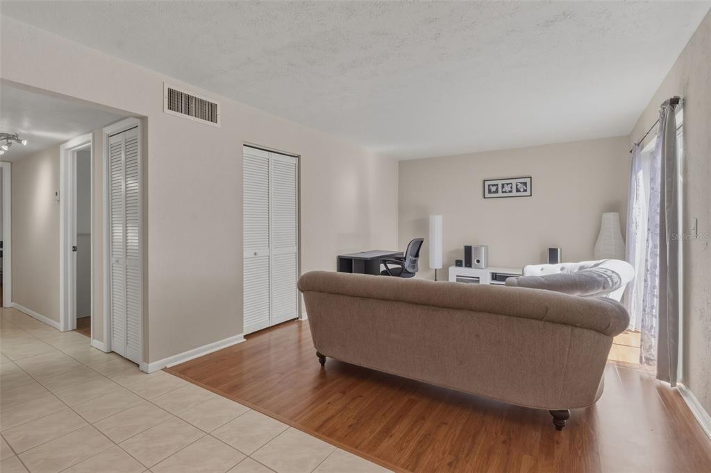 A living room features light-colored walls, wood-look flooring, a beige sofa, and a desk area — 1799 N HIGHLAND AVENUE UNIT 114, CLEARWATER, FL