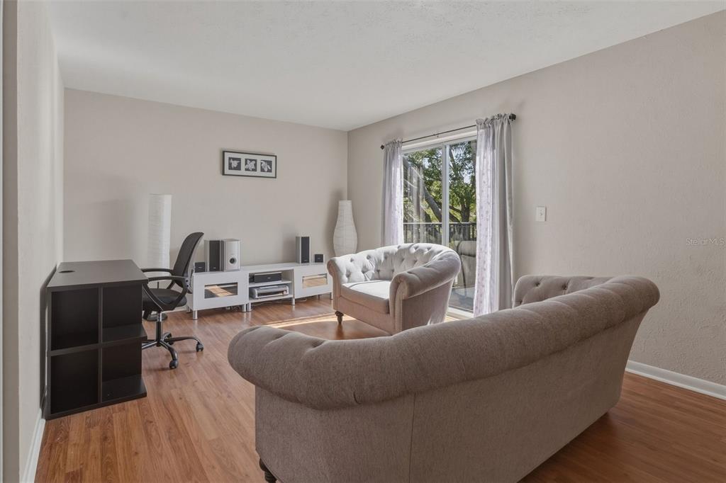 A living room with wood-look flooring, a sofa, an armchair, a desk, and sliding doors — 1799 N HIGHLAND AVENUE UNIT 114, CLEARWATER, FL