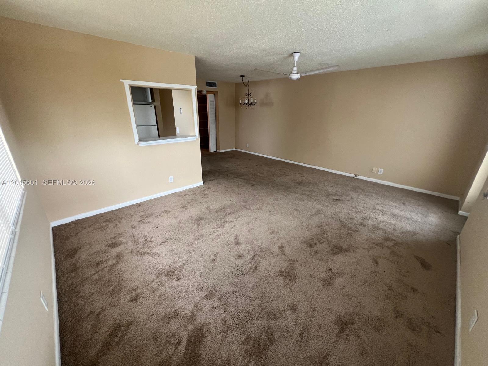An empty living room features beige walls, brown carpeting, a ceiling fan, and a pass-through window — 391 Windsor Q # 0, West Palm Beach FL 33417, WEST PALM BEACH, FL