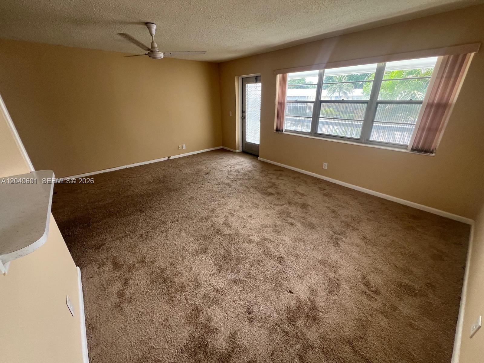 An empty living room features brown carpet, tan walls, a ceiling fan, and a glass door — 391 Windsor Q # 0, West Palm Beach FL 33417, WEST PALM BEACH, FL