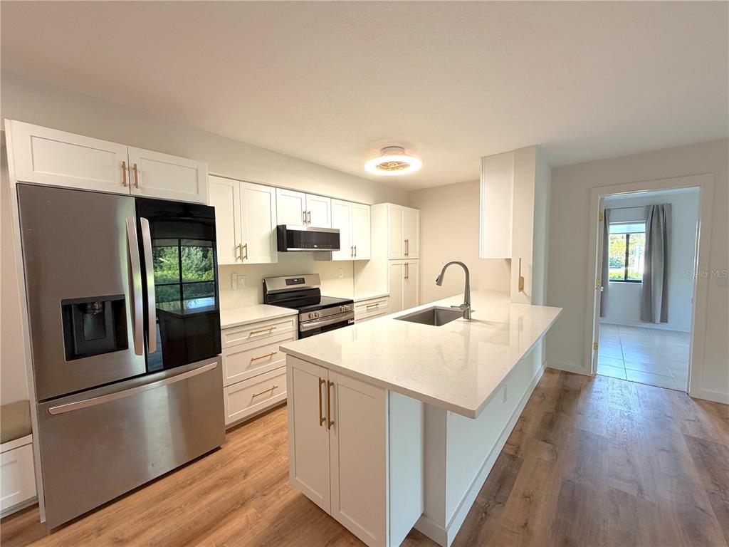 A modern kitchen features white cabinetry, stainless steel appliances, a quartz island, and wood flooring — 2067 HUNTERS GLEN DRIVE UNIT 312, DUNEDIN, FL